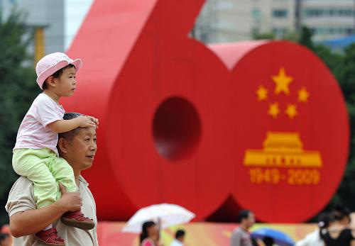 10月1日,一位市民帶著孩子經過福州街頭的新中國成立60周年國慶慶祝活動標志。十一長假期間,各地國慶遊園活動中、廣場綠地上隨處可見孩子們的可愛身影。對純真的兒童而言,十一是祖國母親的生日,也是他們的快樂假期。新華社記者 姜克紅攝